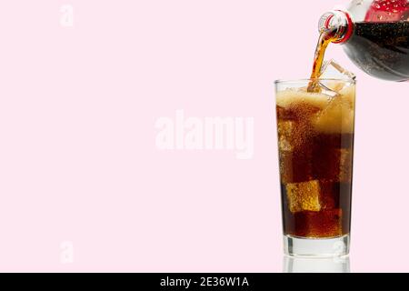 Gießen Sie Cola in Glas mit Eiswürfeln isoliert auf rosa Stockfoto