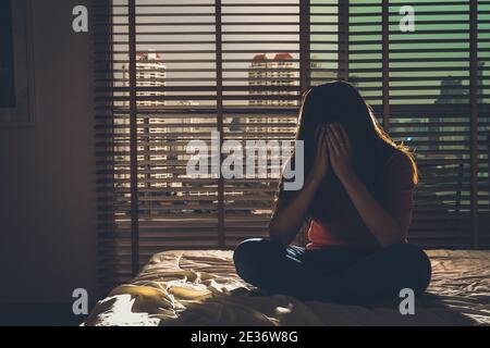 Depressive Frauen sitzen Kopf in den Händen auf dem Bett im dunklen Schlafzimmer mit wenig Licht Umgebung, dramatische Konzept Stockfoto