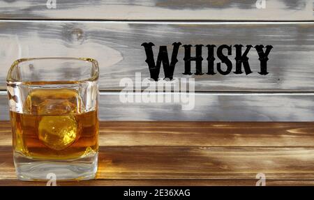 Nahaufnahme eines isolierten Whiskyglases mit Eiswürfel und Holzdielen Hintergrund, Worttext im westlichen Stil (Fokus auf Glas) Stockfoto