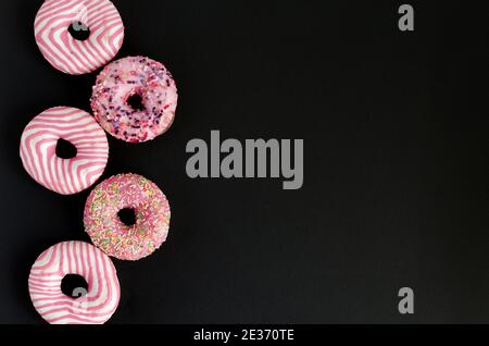 Donuts mit rosa Vereisung liegen auf schwarzem Hintergrund mit Kopie Platz und flache Lage Stockfoto