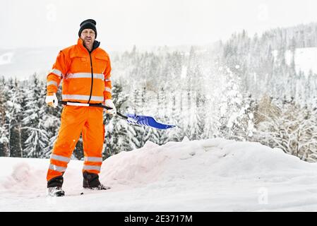 Der kommunale Dienstarbeiter in der Uniform mit der Schaufel klärt den Schnee Im Winter Stockfoto