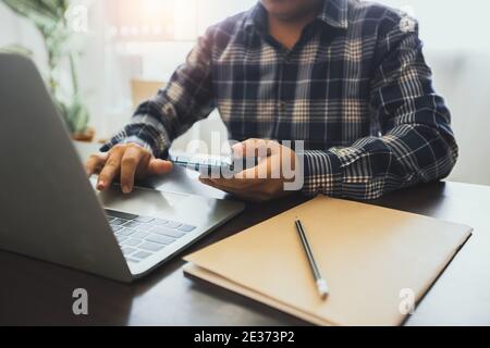 Business mit Technologie-Konzept, Business-Mann hält Telefon und verwenden Laptop auf Arbeitstisch Stockfoto