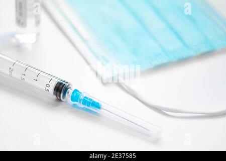 Spritze mit Nadel, Fläschchen und chirurgischer Gesichtsmaske auf einem weißen Tisch bereit verwendet werden. Hintergrund des Covid- oder Coronavirus-Impfstoffs Stockfoto