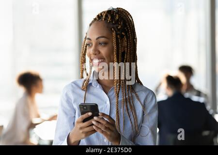Lächelnde ethnische Frau verwenden Handy denken im Büro Stockfoto