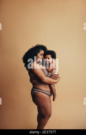 Gesunde Frau hält ihr Baby. Afroamerikanische Familie. Frau mit Post-Baby-Körper mit ihrem Kind. Stockfoto