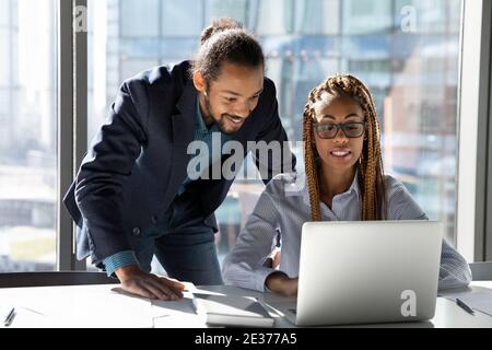 Lächelnde, multiethnische Kollegen arbeiten gemeinsam am Laptop Stockfoto