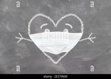 Kinderzeichnung mit Kreide auf der Tafel Herz in ein Schützende antivirale Maske mit Umarmungen valentinstag in covid Stockfoto