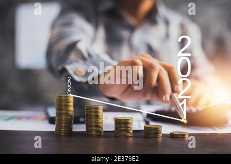 Low-und Down-Geschäft im Jahr 2021, Geschäftsmann zeigt auf Pfeil Grafik auf gestapelt von Münzen, Auswirkungen auf die Verlustleistung, sparen und finanzielle Erwerben c Stockfoto