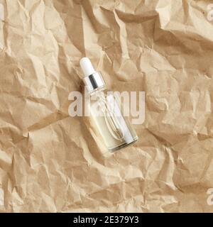 Transparente Serumflasche auf Kraftpapier Draufsicht. Tropferbehälter mit natürlichem ätherischem Öl für die Hautpflege. Stockfoto