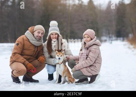 In voller Länge Porträt der glücklichen Familie Blick auf Kamera und lächelnd, während posiert mit kleinen Hund auf freudigen Winterspaziergang, kopieren Raum Stockfoto