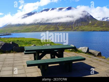 Ein leerer Picknicktisch mit Blick auf den schneebedeckten Berg und den blauen Fjord im Sommer in der Nähe von Olafsfjordur, Island Stockfoto