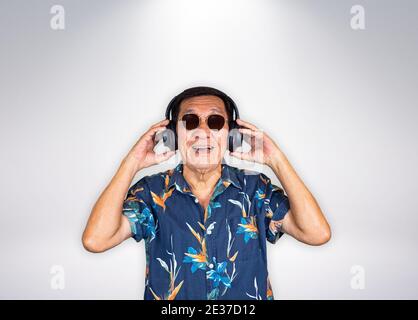 Älterer asiatischer Mann, der mit Kopfhörern Musik hört, mit Sonnenbrille auf grauem Hintergrund Stockfoto
