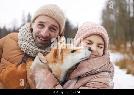 Nahaufnahme Porträt von glücklichen Vater und Mädchen spielen mit Hund beim Spaziergang im Freien zusammen im Winterwald Stockfoto