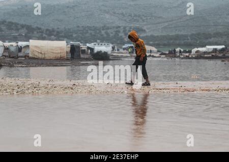 Kafr Aruq, Syrien. Januar 2021. Ein syrisches Kind durchströmt das Hochwasser im überfluteten Tal Amin Lager für Binnenvertriebene, in der Nähe des Dorfes Kafr Aruq. Die Flüchtlingslager im Norden des Gouvernements Idlib sind von extremem Winterwetter bedroht, da sie in den vergangenen Tagen nach heftigen Regenfällen überflutet wurden. Quelle: Anas Alkharboutli/dpa/Alamy Live News Stockfoto