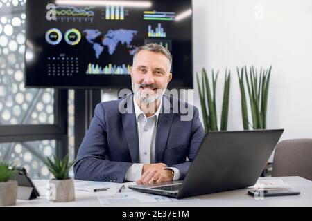 Vorderansicht des reifen mittleren Alters selbstbewusst hoch qualifizierte bärtige Büroleiter oder Chef, in formellen Anzug, posiert vor der Kamera in seinem modernen Büro Stockfoto