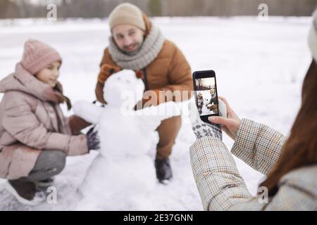 Portrait der jungen Frau Foto von Vater und Tochter Gebäude Schneemann zusammen, Fokus auf Smartphone-Bildschirm, kopieren Raum Stockfoto