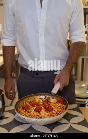Cropped Chef Mann in weißem Hemd Kochen italienische Pasta mit Garnelen auf der Pfanne Stockfoto