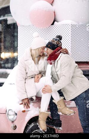 Romantisches Paar küssen, Umarmung, Spaß im Winterwetter sitzen auf rosa Auto während Schneefall Stockfoto