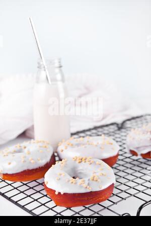Donuts auf dem Backblech glasiert weiße Schokoladencreme oder Glasur und Flasche mit Milch auf dem Hintergrund Stockfoto