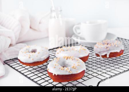 Donuts auf dem Backblech glasiert weiße Schokoladencreme oder Glasur. Flasche mit Milch und Tasse Kaffee auf dem Hintergrund Stockfoto
