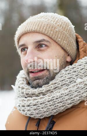 Vertikale Nahaufnahme Porträt von bärtigen reifen Mann im Winter Im Freien trägt Strickmütze und Jacke, während Blick weg bedeckt Im Schnee Stockfoto