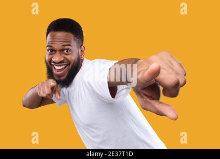 Lustiger afrikanischer Mann posiert mit Zeigefinger auf Kamera, gelber Hintergrund Stockfoto