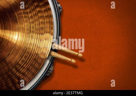 Nahaufnahme eines goldfarbenen Zimbels auf einer Snare-Trommel mit zwei hölzernen Drumsticks auf einem orangefarbenen Samthintergrund mit Kopierraum. Schlaginstrument. Stockfoto