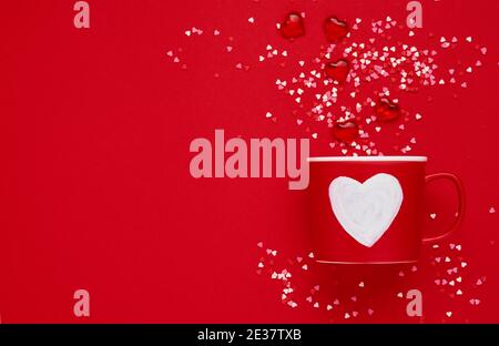 Roter Becher mit Herz, Zucker und Schokoladenherzen auf rotem oder rotem Hintergrund. Flache Lay-Komposition. Valentinstag-Konzept. Draufsicht, Stockfoto