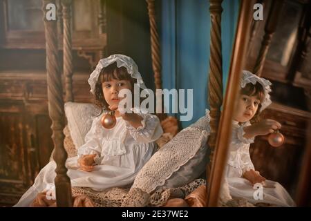 Ein schönes kleines Mädchen in einer weißen Mütze sitzt in Ein weißes Vintage-Nachtkleid Stockfoto