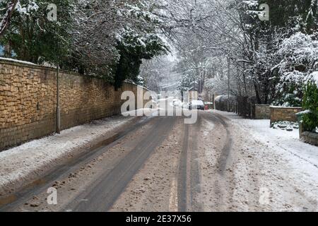 Blick auf eine schneebedeckte, von Bäumen gesäumte Boston Spa High Street mit Spuren, die von Fahrzeugen erstellt wurden, die entlang der Straße fahren Stockfoto