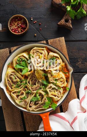 Fleischteig rollt mit Fleisch oder faulen Knödeln in einer gusseisernen Pfanne auf einem alten rustikalen dunklen Holzhintergrund. Draufsicht. Stockfoto