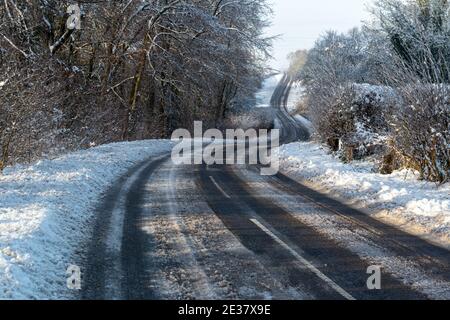 Sonniger Blick auf eine schneebedeckte Landstraße, die sich durch Bäume schlängelt in Bramham, West Yorkshire Stockfoto