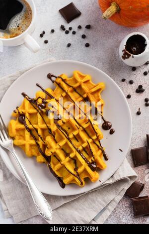 Kürbiswaffeln mit Schokolade und Puderzucker, serviert zum Frühstück auf hellem Hintergrund und altem rustikalen Frühstückstisch. Selektiver Fokus. Stockfoto