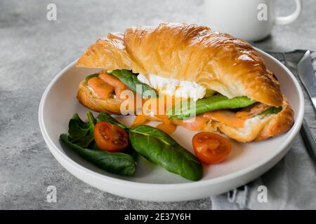 Croissant-Sandwich mit Quark, Lachs, Spinat. Pochiertes Ei. Gesundes Frühstück Stockfoto