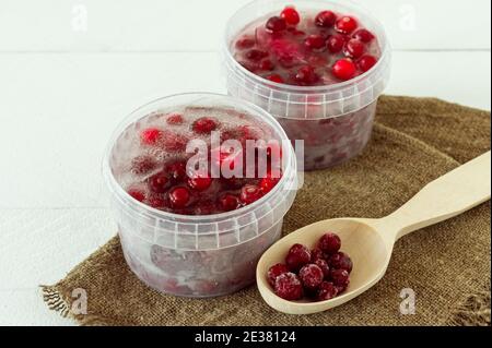 Gefrorene gesunde Preiselbeeren in einem Plastikbehälter mit Eiswürfel auf Holzgrund. Stockfoto