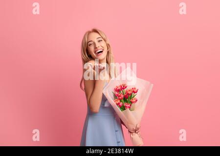 Fröhliche junge Dame mit schönen Frühlingsblumen lachen und suchen Bei der Kamera auf pinkem Studiohintergrund Stockfoto