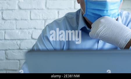 Arzt in einem Krankenhausbüro mit einer Gesichtsmaske und Schutzhandschuhe mit einem Laptop Stockfoto