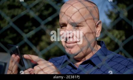 Bild mit einer älteren Person hinter einem metallischen Zaun mit Ein Smartphone Stockfoto