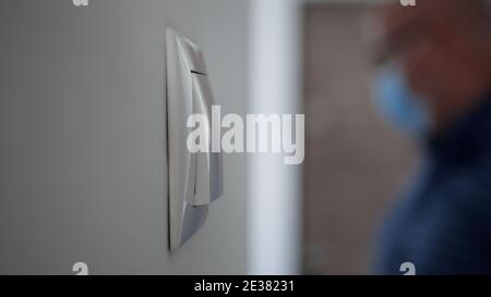 Ein Lichtschalter an der Wand und eine verschwommene Person Im Hintergrund trägt medizinische Gesichtsmaske Eingabe in das Büro Stockfoto