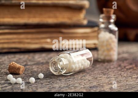Eine Flasche homöopathischer Pillen auf einem hölzernen Hintergrund, mit alten Büchern im Hintergrund Stockfoto