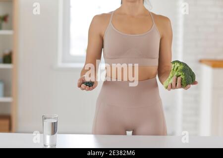 Unbekannte Frau hält Brokkoli und Spirulina, während sie in der Küche neben Glas Wasser steht. Stockfoto