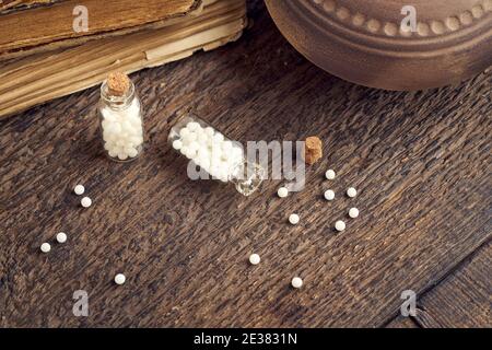 Eine Flasche homöopathischer Pillen auf einem Tisch, mit alten Büchern im Hintergrund Stockfoto