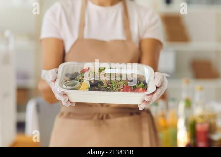 Nahaufnahme von Lebensmitteln auf dem Plastikbehälter zum Mitnehmen in den Händen einer gesichtslosen Frau, die Handschuhe trägt. Stockfoto