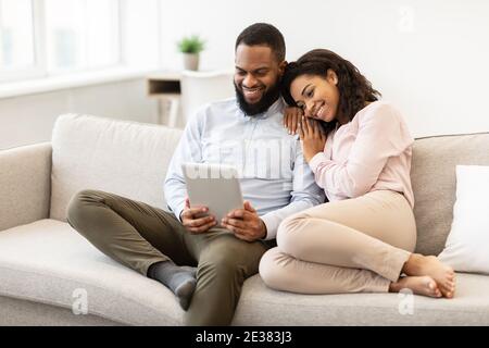 afroamerikanisches Paar sitzt auf der Couch, mit Tablet Stockfoto