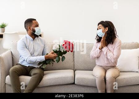 Schwarzer Mann in medizinischer Maske, der seiner Frau Rosen gibt Stockfoto