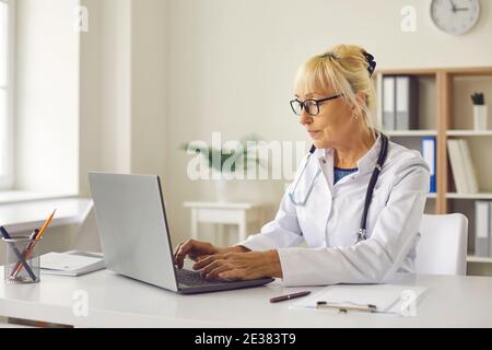 Der Arzt sitzt vor einem Laptop und gibt die Diagnose des Patienten in eine elektronische Datenbank ein. Stockfoto