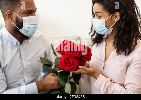 Schwarzes Paar in medizinischen Masken mit Datum, hält Rosen Stockfoto