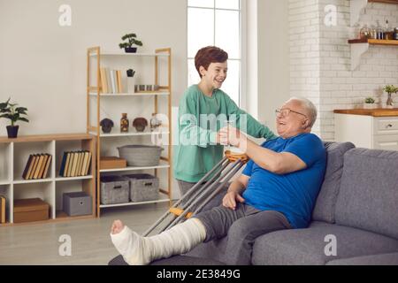 Glücklicher Enkel hilft Großvater, der Bein während der Genesung gebrochen hat Zeit zu Hause Stockfoto