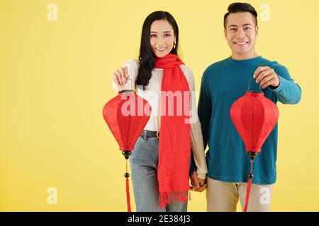 Fröhliche vietnamesische Freund und Freundin im Winter Pullover Hände halten Und zeigt rote Papier Lanters für Tet Feier Stockfoto