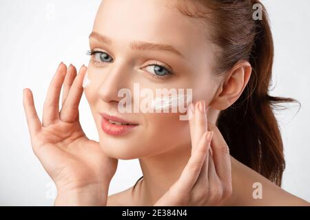 Rothaarige Junge Frau, Die Creme Auf Gesicht, Studioaufnahme, Nahaufnahme Anwendet Stockfoto